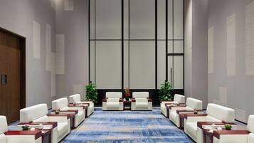 Un salón de conferencias con una larga mesa, sillas blancas y pequeñas mesas con centros de flores.