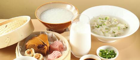 A table with various food items including a bowl of soup, a plate of fruit, a cup of coffee, and a plate of pastries.