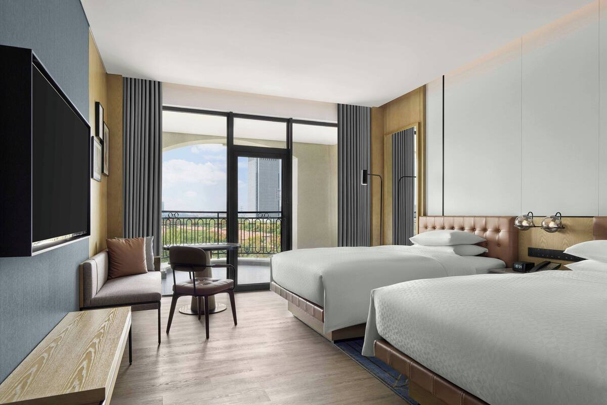 Une chambre d’hôtel avec deux lits, un canapé, une petite table et un balcon donnant sur la ville.