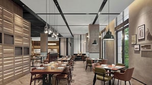 A modern dining area with wooden tables and chairs, pendant lighting, and large windows providing natural light.