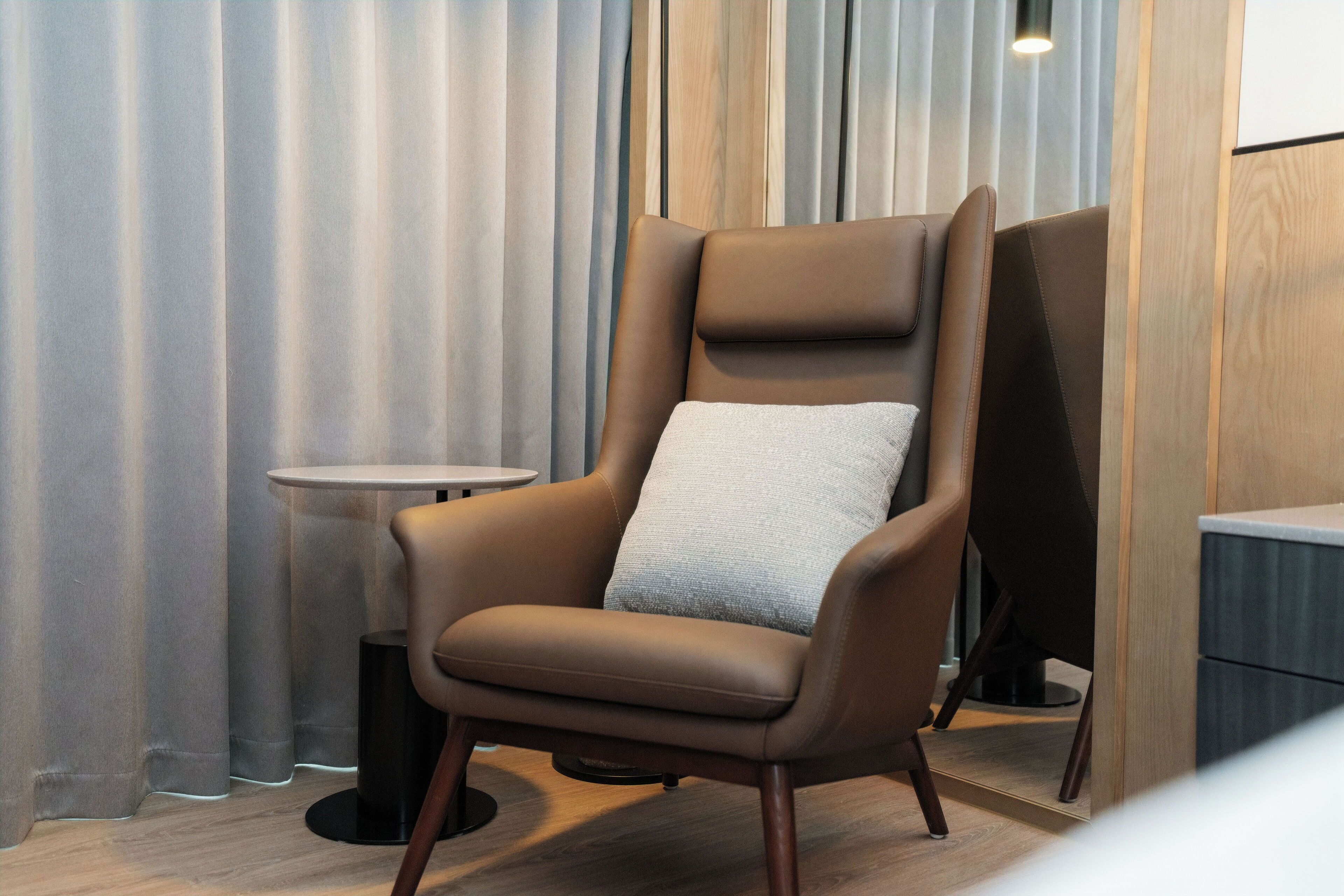 A modern armchair with a cushion, positioned in a room with wooden flooring and a small round table.