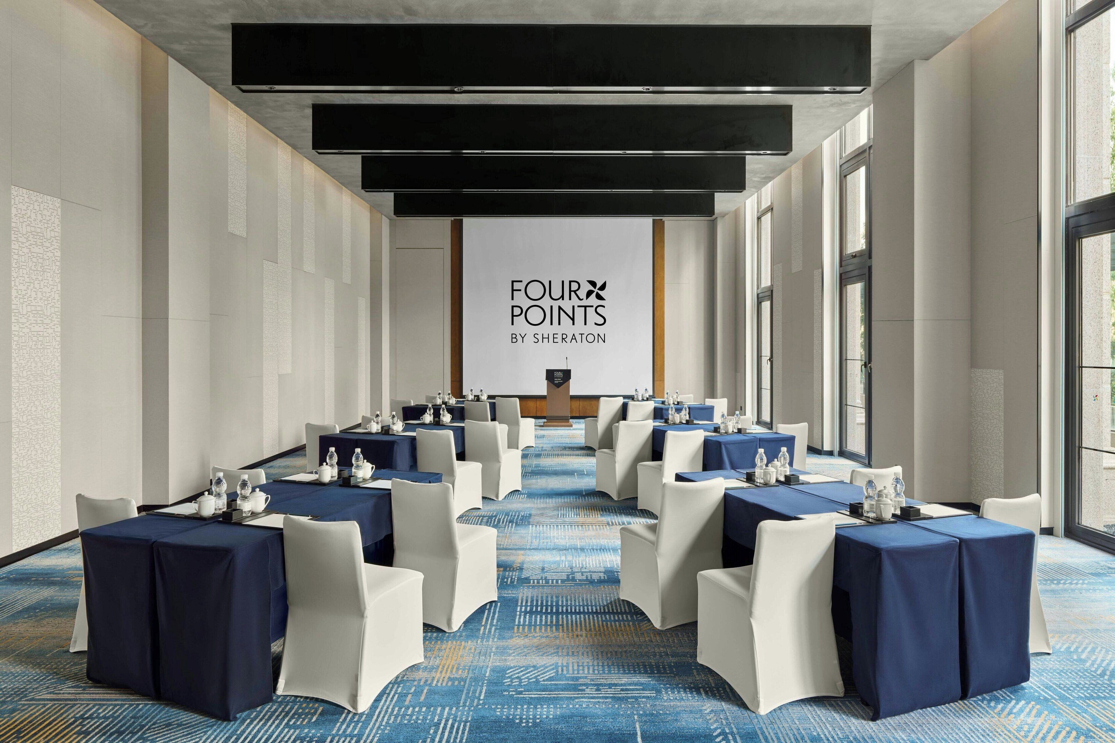 Une salle de conférence avec une longue table préparée pour une réunion, des chaises blanches et une moquette bleue.