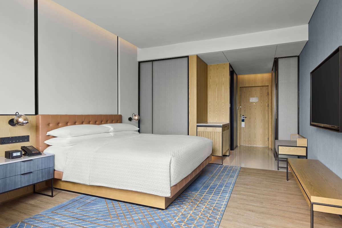 Une chambre d’hôtel moderne, dotée d’un grand lit, de tables de chevet, d’un bureau et d’une télévision.