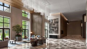 A spacious lobby with a large potted plant, seating area, and a modern chandelier.