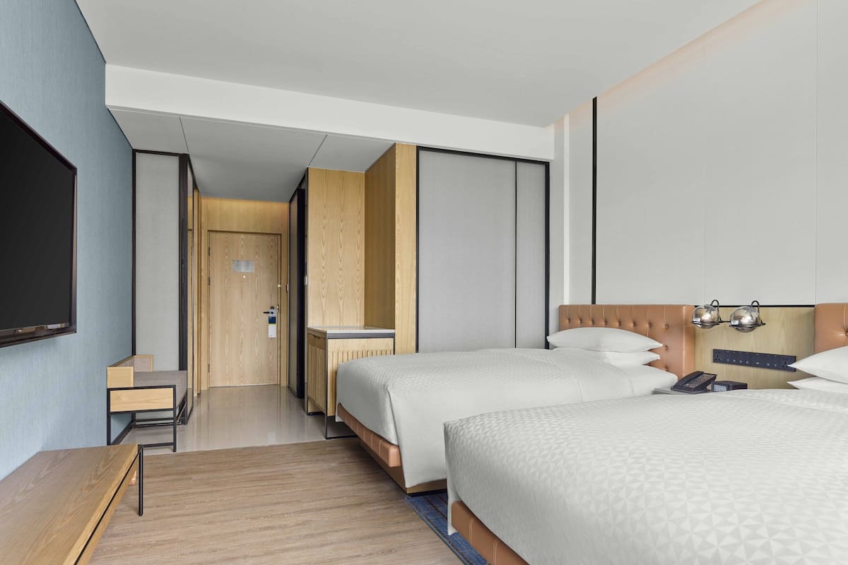 Une chambre d’hôtel moderne équipée de deux lits, d’un bureau et d’une télévision.