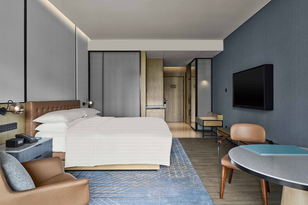 Une chambre d’hôtel moderne équipée d’un grand lit, d’un bureau, d’une chaise, d’un téléviseur à écran plat et d’un téléphone sur la table de chevet.