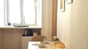 Spiseområde med et bord dækket til to personer, et vindue med gardiner, en hængende lampe og billeder i rammer på væggen.