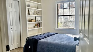 Un dormitorio con cama, ventilador de techo, ventana y estantería.
