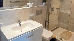 Un bagno moderno con uno specchio grande, un lavandino bianco, un WC e una zona doccia con pareti in vetro.