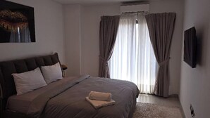 Una camera da letto con un letto grande, un comodino, una TV a parete e una finestra con tende.