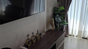 Un soggiorno moderno con una TV a schermo piatto montata sulla parete, un mobile TV in legno scuro con oggetti decorativi e un'ampia finestra con tende.