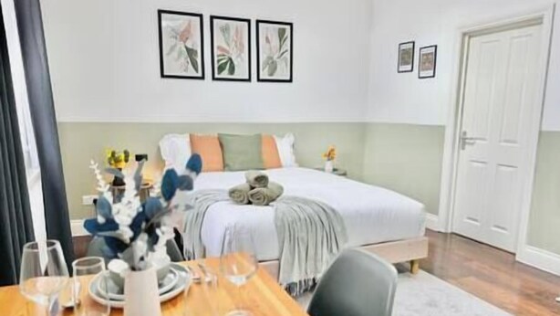 Une chambre d’hôtel avec un lit, une table à manger dressée avec des assiettes et des verres, et trois tableaux encadrés accrochés au mur.