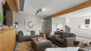 Un salon moderne avec des canapés gris, un meuble en bois, une grande peinture abstraite et un tapis à motifs.