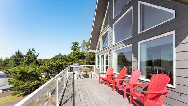 Une terrasse en bois avec des fauteuils Adirondack rouges, un barbecue et une table.