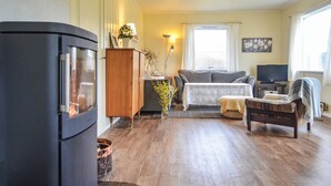 A cozy living room with a wood-burning stove, a sofa, a chair, and a television. - Lovely home in Sørbøvåg (Sørbøvåg)