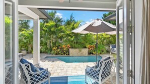 A covered outdoor area with a pool, white wicker furniture, and a ceiling fan.