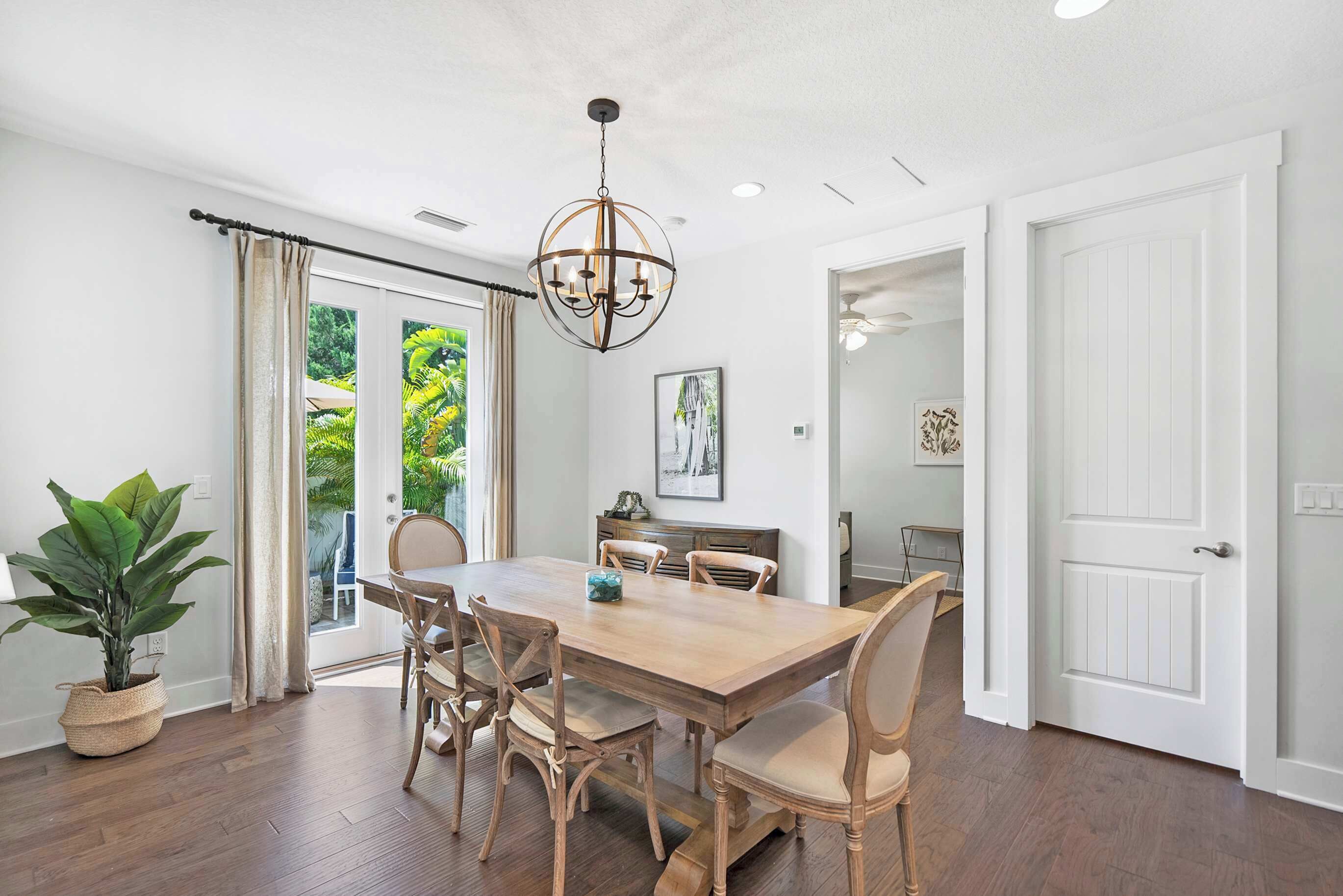 A dining room with a wooden table, six chairs, a chandelier, and a potted plant.