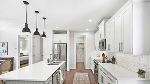 A modern kitchen with white cabinetry, a large island, pendant lighting, and a patterned rug.