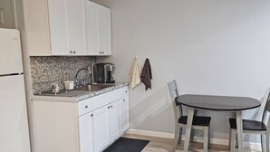 Cocina compacta con armarios blancos, cafetera y una mesa de comedor con sillas.