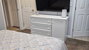 Un dormitorio con cama, cómoda, televisor y puerta.