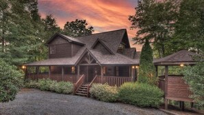 A rustic log cabin with a covered porch, a staircase leading to the entrance, and a small wooden structure to the right. - Black Bear Hollow - Gather, Play, Relax, Repeat (Blue Ridge)