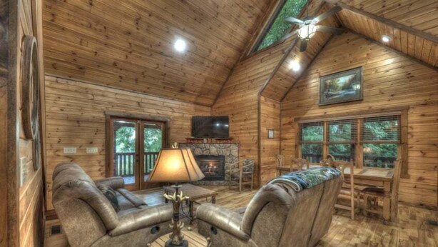 A log cabin interior with a fireplace, leather sofas, and a dining area. - Black Bear Hollow - Gather, Play, Relax, Repeat (Blue Ridge)
