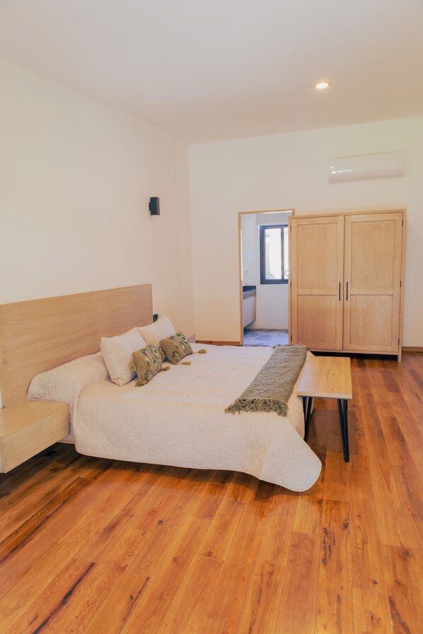 Un dormitorio con una cama de madera, una mesita de noche de madera, un armario de madera y un banco de madera.