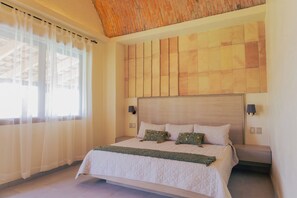 Un dormitorio con una cama grande, cabecera con estampado geométrico, dos lámparas de pared y cortinas de gasa.