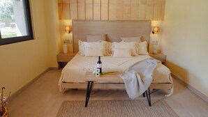 A bedroom with a wooden headboard, a bedside table with a bottle and glasses, and a bed with multiple pillows. - Vid de Luna (San Miguel de Allende)