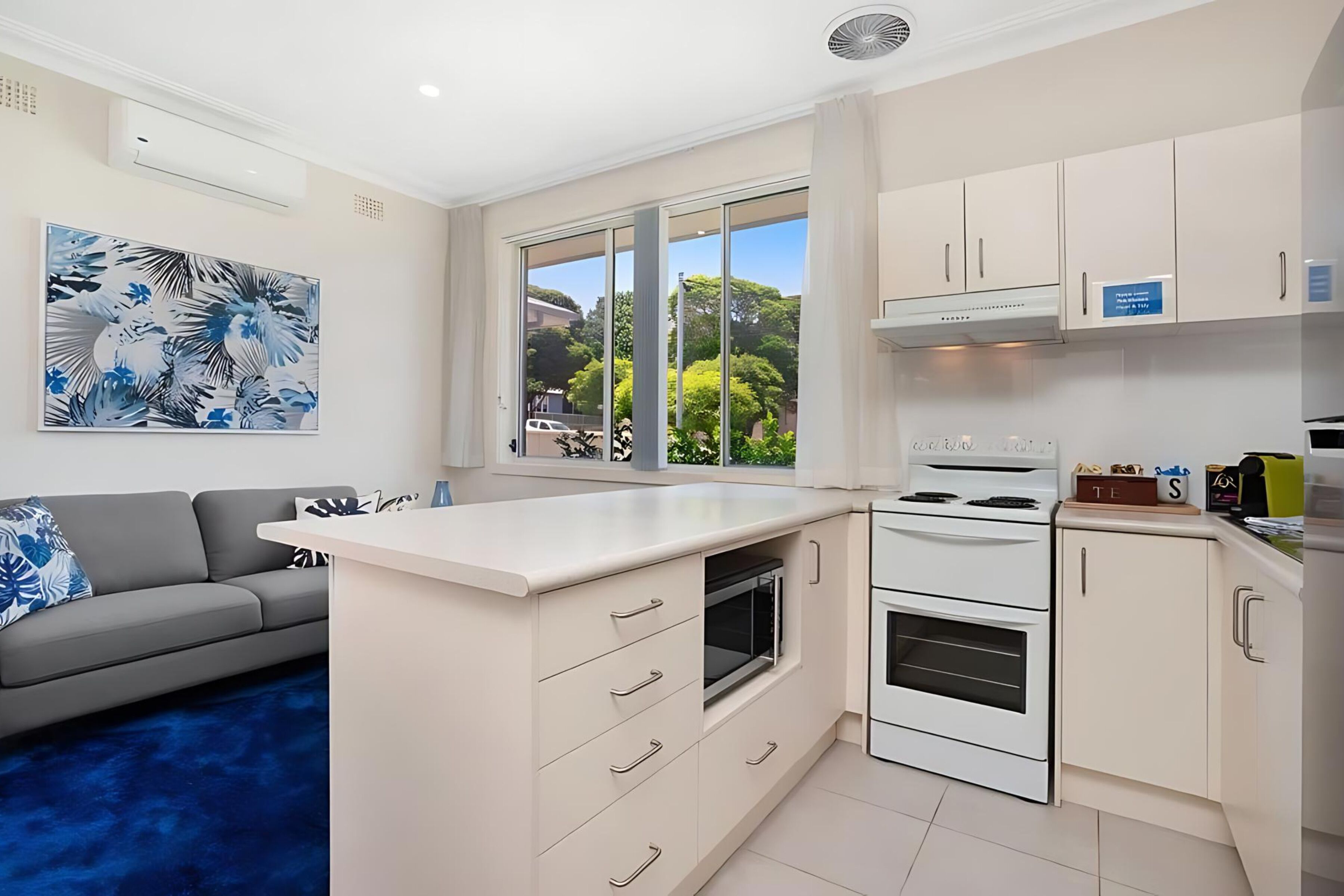A modern kitchen with white cabinets, a built-in oven, and a large window offering a view of greenery outside.