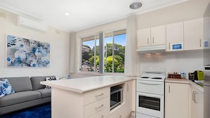 Una cocina moderna con armarios blancos, horno integrado y un amplio ventanal con vistas a la vegetación.