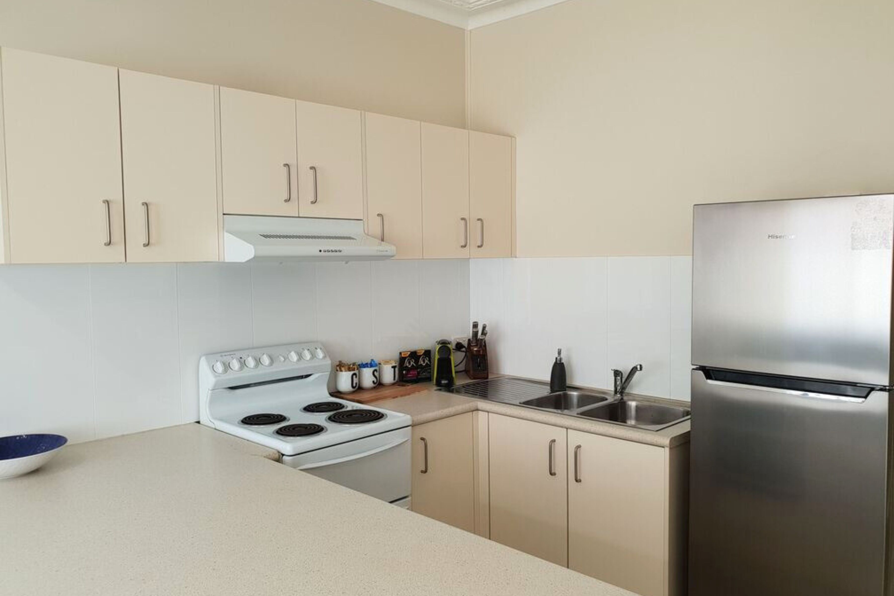 A modern kitchen with beige cabinets, a stainless steel refrigerator, a white stove, and a sink.