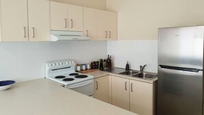 Una cocina moderna con armarios color beige, un refrigerador de acero inoxidable, una estufa blanca y un fregadero.