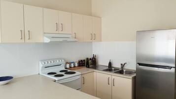 A modern kitchen with beige cabinets, a stainless steel refrigerator, a white stove, and a sink.