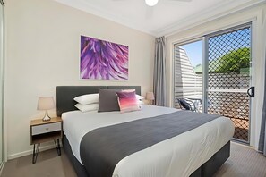 A modern hotel room with a large bed, a nightstand with a lamp, a ceiling fan, and a large window with a view of the outside. - Prickly Pear Stays in Mayfield (Mayfield)