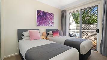 A hotel room with two beds, a ceiling fan, a large window with a view, and a table outside.