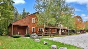 A rustic cabin with a wooden exterior, a porch, and a gravel driveway.