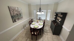 A dining room with a round table, six chairs, a chandelier, and a painting on the wall.