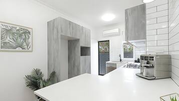 Una cocina moderna con encimeras blancas, horno empotrado y cafetera.