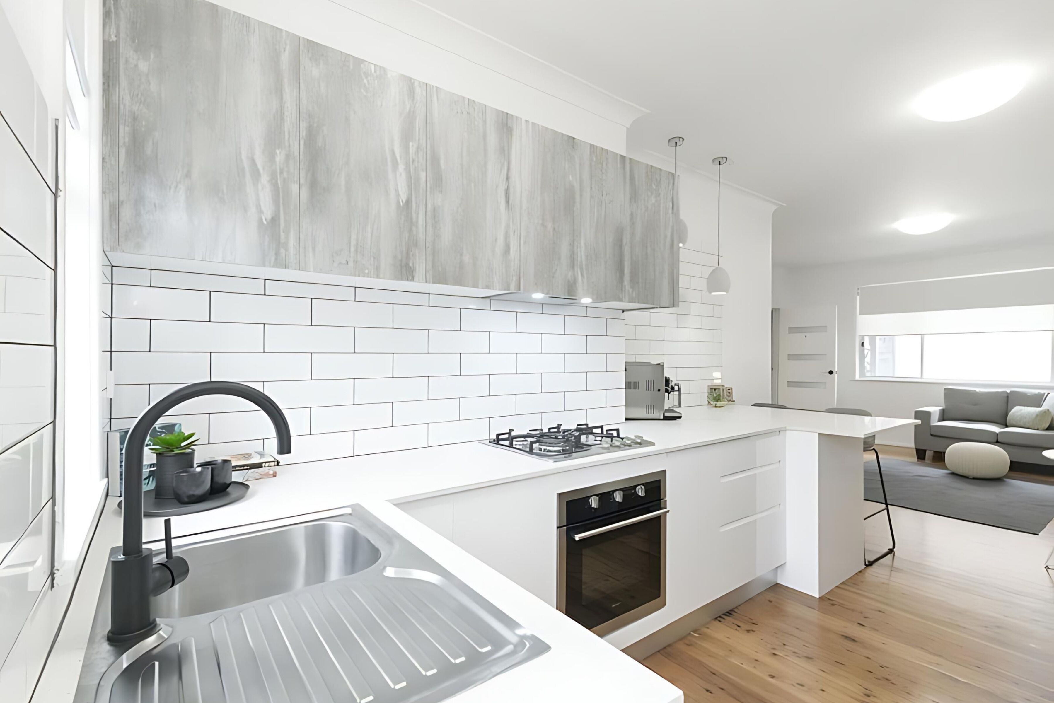Una cocina moderna con armarios blancos, un lavamanos de acero inoxidable, un horno empotrado y un salpicadero gris.
