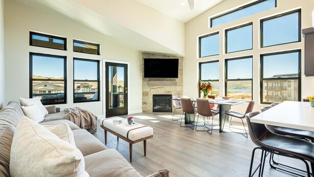 A spacious living room with a large sofa, a dining area with a table and chairs, a fireplace, and large windows offering a view of the landscape. - Free Ski Shuttle- Minutes to Ski and Lake, Community Clubhouse-Pool & Hot Tub (Heber City)