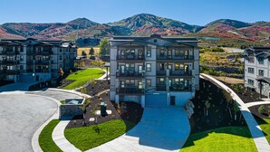 A modern multi-story residential building with a curved driveway, landscaped areas, and a mountainous backdrop. - Free Ski Shuttle- Minutes to Ski and Lake, Community Clubhouse-Pool & Hot Tub (Heber City)