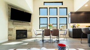 A modern living room with a stone fireplace, a dining area with a table and chairs, a kitchen with dark cabinets, and a large window with multiple panes. - Free Ski Shuttle- Minutes to Ski and Lake, Community Clubhouse-Pool & Hot Tub (Heber City)