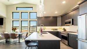 A modern kitchen with a large island, dark cabinetry, stainless steel appliances, and a dining area with a view. - Free Ski Shuttle- Minutes to Ski and Lake, Community Clubhouse-Pool & Hot Tub (Heber City)