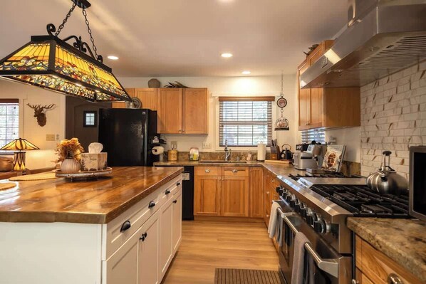 A kitchen with wooden cabinets, a black refrigerator, a gas stove, and a hanging light fixture.