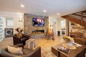 A living room with a stone fireplace, a television mounted above it, and a cozy seating area with leather sofas and a coffee table.