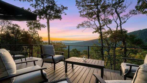 A deck with outdoor seating, a glass table, and a view of the landscape.