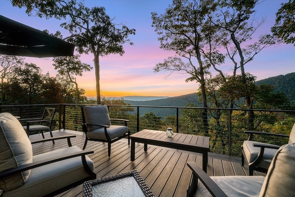A deck with outdoor seating, a glass table, and a view of the landscape.