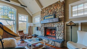 A cozy living room with a stone fireplace, leather furniture, and large windows.
