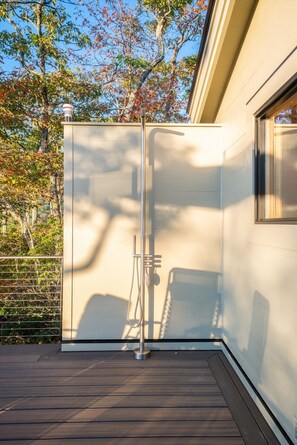 A modern outdoor shower area with a metal structure, a wooden deck, and a building with a window.